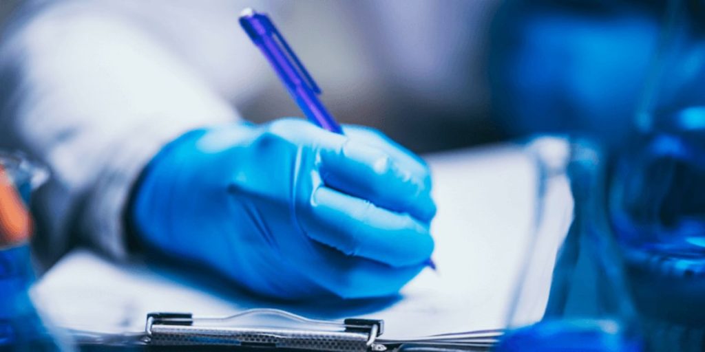 a person wearing a white doctors coat and blue rubber gloves writing on a clipboard
