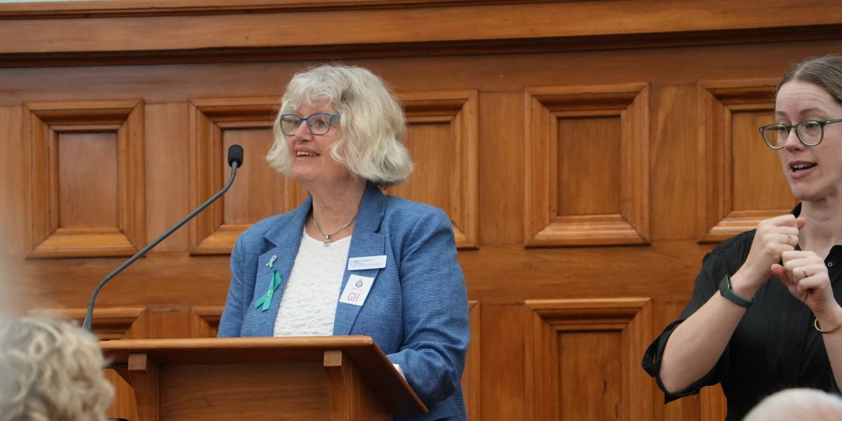 Ele standing at a lectern at Parliament delivering a speech
