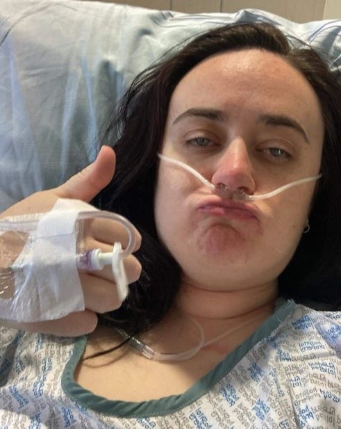 Chloe sitting in a hospital bed with a nose tube in doing the thumbs up
