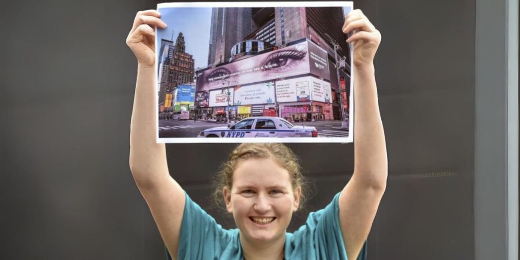 Our Founder Jane holding up a photo showing a billboard raising awareness of ovarian cancer in times square