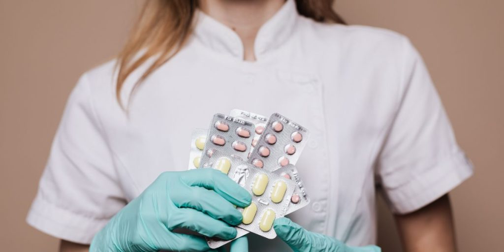 a woman in a lab coat holding some packets of pills